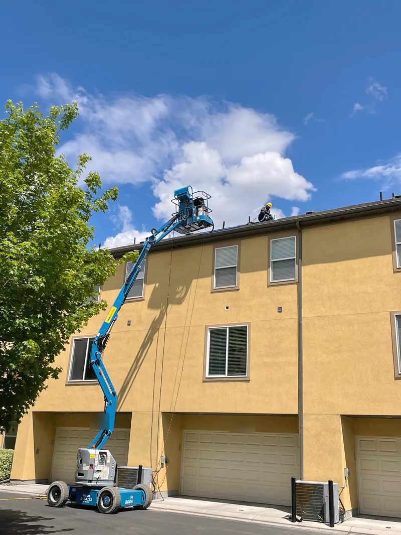 Boom lift reaching roof dryer vents on a three-story building